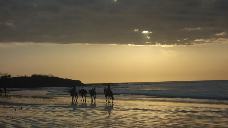 Reiter am Strand von Tamarindo bei Sonnenuntergang unter Wolken